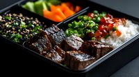 Korean beef bulgogi in black bento box with steamed rice, sesame quinoa, fresh vegetables and green onions. Traditional Asian lunch meal prep served in portion container.