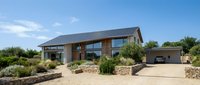 Modern sustainable home with solar panels and natural stone landscaping under clear blue sky for eco-friendly architecture and green building concepts.