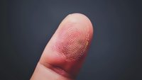 Close-up macro shot of fingerprint pattern on human finger showing detailed ridges and unique biometric identification marks against dark background.