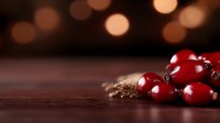 Fresh red cranberries scattered on dark wooden surface with warm bokeh lights in background creating festive holiday atmosphere.