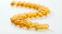 Golden omega-3 fish oil capsules arranged in curved line on white background for health and wellness supplement marketing materials.