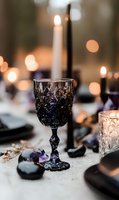 Elegant dark purple crystal wine glass on white tablecloth with glowing candles and amethyst crystals creating mystical atmosphere for romantic dinner or gothic wedding decor.
