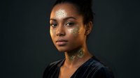 Young African American woman with intricate golden henna tattoos on face and neck against dark background for beauty and cultural art concepts.