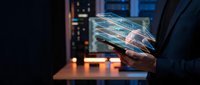 Businessman holding transparent digital tablet displaying holographic data visualization in server room environment with glowing lights.