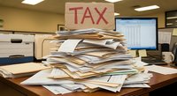 Overwhelming pile of tax documents and paperwork stacked high on office desk with TAX sign, representing tax season preparation and financial burden.