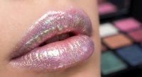 Glossy pink lips with shimmery glitter lipstick and colorful makeup palette in background for beauty and cosmetics concepts.