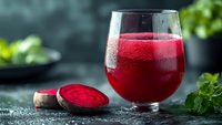 Fresh beetroot juice in glass with sliced beet root on dark background, healthy detox drink for natural nutrition and wellness.