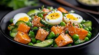 Fresh spinach salad with smoked salmon, hard-boiled eggs, and sesame seeds in black bowl. Healthy protein-rich meal for breakfast, lunch or dinner menu.