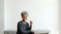 Senior woman with gray hair and warm smile wearing dark gray sweater, seated against white background, suitable for healthcare, wellness, lifestyle and portrait design projects.