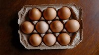 Fresh brown chicken eggs arranged in cardboard carton on wooden surface, top view composition showing natural organic food and farm produce.