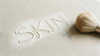 Makeup brush with bristles creating the word skin on textured surface, representing skincare, cosmetics, and beauty product design applications.