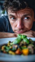 Close-up portrait of man with intense expression looking at healthy vegetable dish, illustrating food cravings or dietary choices.