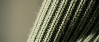 Green knitted wool fabric texture with ribbed pattern showing detailed fiber structure and natural textile weave for fashion and craft projects.