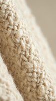 Close-up macro shot of cream colored knitted wool fabric showing detailed cable stitch pattern and soft natural fiber texture for cozy winter fashion designs.