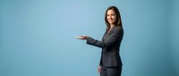 Professional businesswoman in dark suit presenting with open hand gesture on blue background for corporate marketing materials.