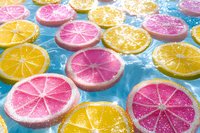 Colorful citrus slices with sugar coating arranged on blue background, featuring pink grapefruit and yellow lemon halves for summer beverage, candy, confectionery, and food styling projects.