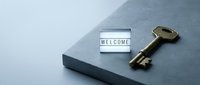 Vintage brass key and glowing welcome sign on dark stone surface, symbolizing hospitality, new home, hotel check-in, or real estate concept.