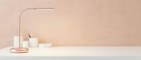 Minimalist workspace with rose gold desk lamp, white candles, and neutral beige background for modern interior design projects.
