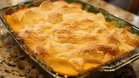 Homemade peach cobbler dessert in glass baking dish with golden brown crust and bubbling fruit filling, fresh from oven, traditional southern comfort food.
