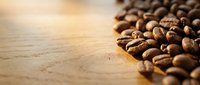Roasted coffee beans scattered on wooden surface with warm natural lighting, suitable for cafe, beverage, and food industry marketing materials.