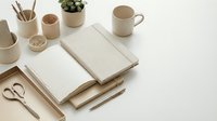 Minimalist beige workspace with open notebook, ceramic mug, plant and office supplies on white desk for productivity and organization.