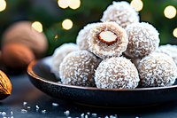 Homemade coconut chocolate truffles with almonds on dark plate against blurred holiday lights background, selective focus on sweet dessert balls.