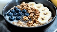 Healthy breakfast bowl with oatmeal, fresh blueberries, sliced banana, crushed walnuts and chia seeds in black ceramic bowl, close up view for food blogs.