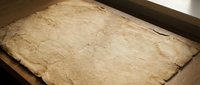 Ancient weathered parchment manuscript with torn edges and aged texture lying on wooden surface for historical document design projects.