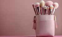 Professional makeup brushes set in pink leather cosmetic bag with tassels against rosy background, soft focus beauty accessories for professional artists.