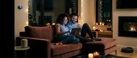 Happy couple relaxing on sofa using tablet computer in cozy living room with fireplace and warm lighting for evening entertainment at home.