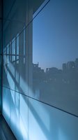Modern office building glass facade with blue evening light reflecting urban cityscape in background for corporate architecture design.