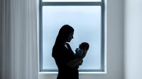Mother holding newborn baby in silhouette against bright window light creating tender bonding moment in modern home interior for family concepts.