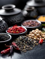 Aromatic spices and dried chili peppers in ceramic bowls on dark background, selective focus on scattered black peppercorns and red chilies for cooking.