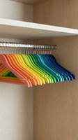 Colorful rainbow hangers arranged in spectrum order inside wooden wardrobe closet for organized clothing storage and home organization solutions.