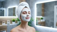 Young woman with white facial mask and towel on head relaxing in modern spa bathroom with closed eyes enjoying skincare treatment routine.