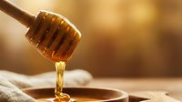 Golden honey dripping from wooden dipper into bowl on rustic table with warm sunlight creating natural organic food photography for culinary content.