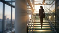 Professional businesswoman climbing modern glass staircase in corporate office building during golden hour sunset with city skyline view.