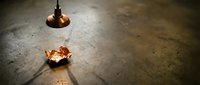 Young male with South Asian appearance in distressed state lying on concrete floor beneath hanging light bulb, depicting despair and hardship.