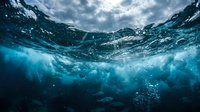 Underwater ocean wave view with sunlight rays penetrating through crystal clear blue water surface creating dramatic lighting effects and bubbles.