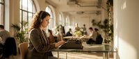 Young professional woman typing on vintage typewriter in modern coworking space with natural sunlight and plants creating inspiring creative workspace atmosphere.
