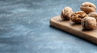 Fresh whole and cracked walnuts on wooden cutting board against dark textured background with copy space. Food photography for healthy eating concept.