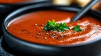 Rich tomato soup with fresh herbs and black pepper in dark bowl ready to serve for comfort food dining and restaurant menu photography.