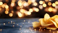 Crispy potato chips on dark surface with golden bokeh lights in background creating festive atmosphere for food photography and holiday designs.