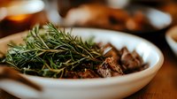 Fresh rosemary sprigs and roasted mushrooms in white ceramic bowl on wooden surface, selective focus with warm ambient lighting creates cozy atmosphere.