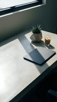 Minimalist workspace with laptop, succulent plant in geometric pot, and iced coffee on white marble desk by window with natural light.