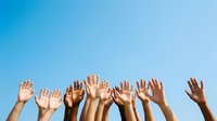 Multiple diverse hands raised together against clear blue sky, representing unity, teamwork, collaboration, volunteer work, community support, and collective action for charitable causes.