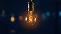 Vintage Edison bulb with warm glowing filament against dark blue background with bokeh lights, suitable for energy, innovation, and creative concept designs.