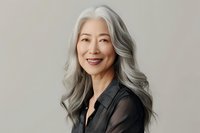 Elegant mature Asian woman with long silver gray hair and natural makeup wearing black blouse, smiling confidently against neutral background. Professional portrait.