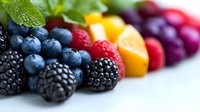 Fresh mixed berries and mango chunks arranged in colorful rows with mint leaves, showcasing vibrant natural colors and textures on white background for food photography.