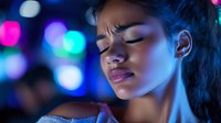 Young Asian woman with eyes closed, experiencing discomfort or stress, surrounded by vibrant neon blue and pink bokeh lights. Suitable for mental health, wellness, and nightlife concepts.